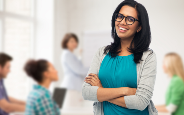An employee wearing glasses is standing in front of others while smiling.