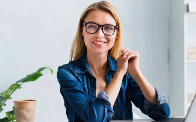 A woman wearing glasses is sitting by herself and smiling.