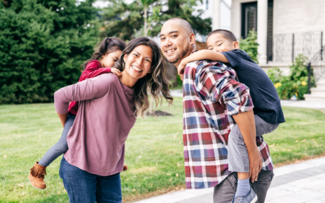 A family together smiling! The mom is holding a little girl on her back. The dad is holding the little boy on his back.