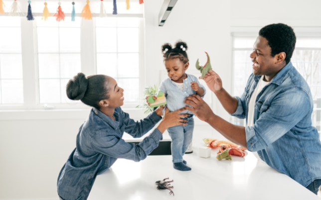 A man and woman are smiling holding their little girl on the countertop.