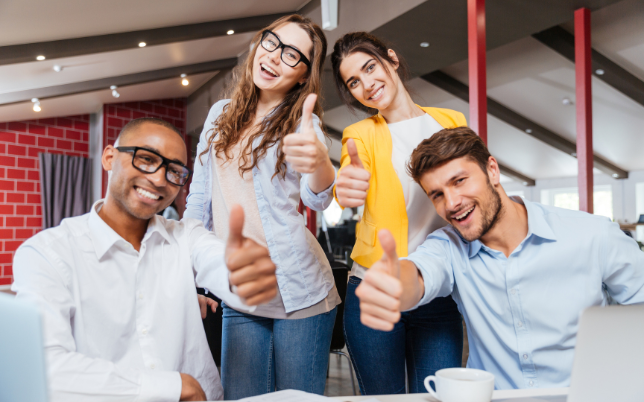 A group of coworkers smiling with their thumbs up. Two of the four employees are wearing glasses.