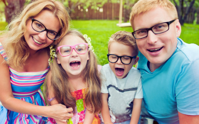 A happy family of four, smiling and wearing glasses outside.